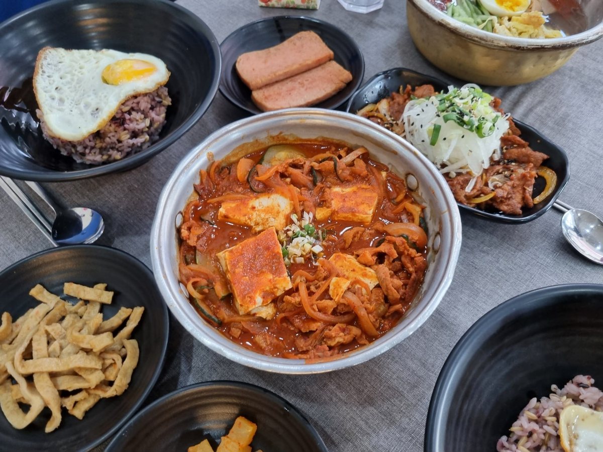 짜글이를 가운데 두고 계란프라이 올린 잡곡밥·스팸·제육볶음·반찬을 차린 한 상